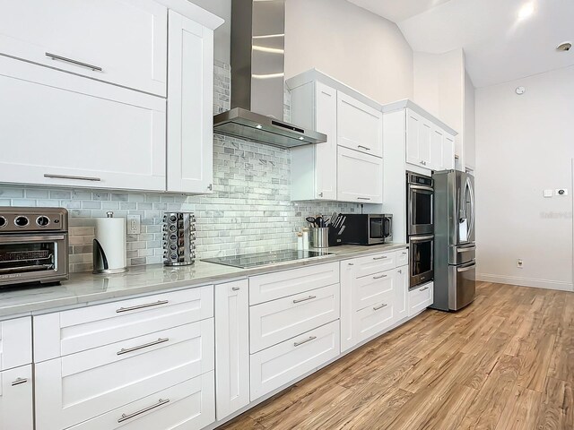 kitchen featuring appliances with stainless steel finishes, tasteful backsplash, wall chimney exhaust hood, light hardwood / wood-style flooring, and white cabinets