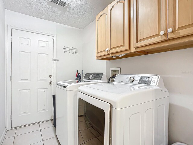 laundry area featuring cabinets, washing machine and dryer, a textured ceiling, and light tile patterned floors