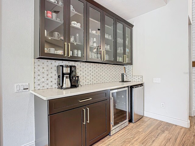 bar with dark brown cabinetry, stainless steel refrigerator, wine cooler, tasteful backsplash, and light hardwood / wood-style flooring