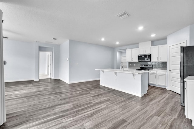 kitchen with an island with sink, a kitchen bar, decorative backsplash, white cabinets, and appliances with stainless steel finishes