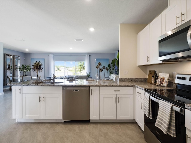 kitchen featuring kitchen peninsula, white cabinets, appliances with stainless steel finishes, dark stone counters, and sink