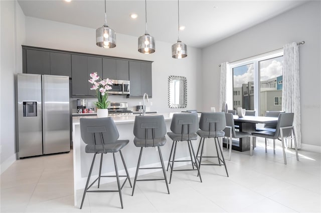 kitchen with a kitchen island with sink, a kitchen breakfast bar, appliances with stainless steel finishes, and pendant lighting