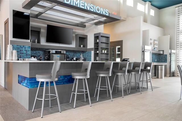 kitchen with kitchen peninsula, stainless steel fridge, tasteful backsplash, a kitchen bar, and a high ceiling