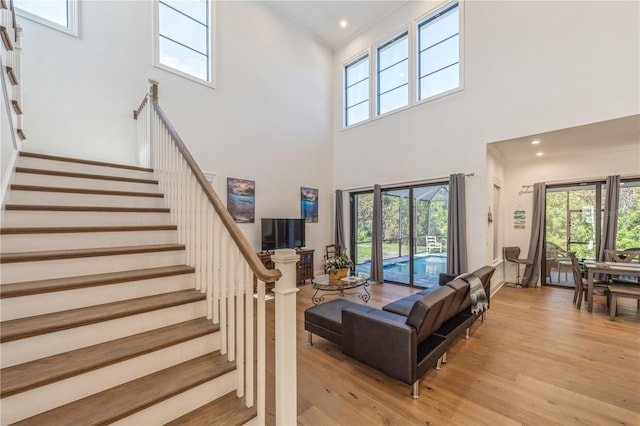 living room with a high ceiling, ornamental molding, and light hardwood / wood-style floors