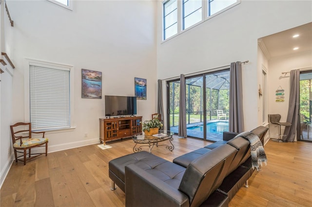 living room with a towering ceiling, ornamental molding, and light hardwood / wood-style flooring