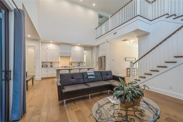 living room with ornamental molding, light wood-type flooring, sink, and a high ceiling