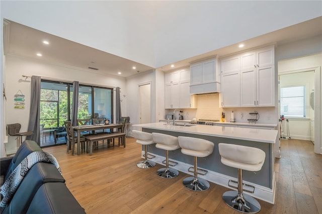 kitchen with sink, a breakfast bar, backsplash, white cabinets, and light wood-type flooring