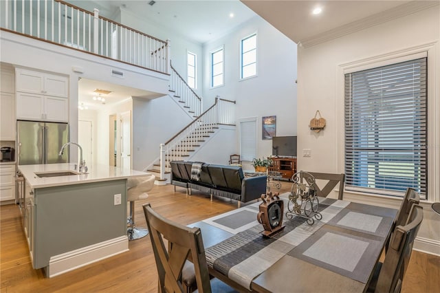 dining space with light wood-type flooring, sink, ornamental molding, and a towering ceiling