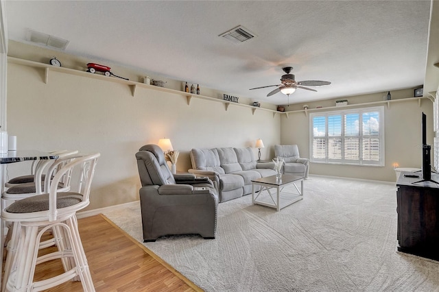 living room with a textured ceiling, wood-type flooring, and ceiling fan