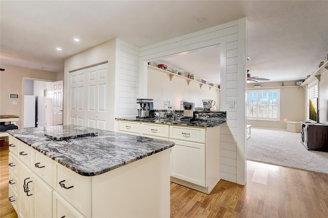 kitchen featuring ceiling fan, dark stone counters, light hardwood / wood-style floors, and a kitchen island