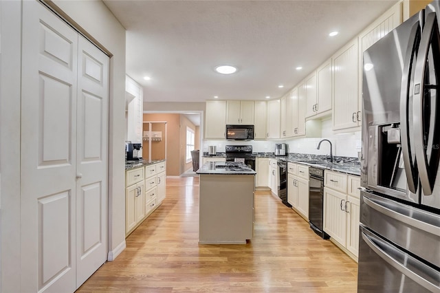 kitchen featuring black appliances, sink, a kitchen island, light hardwood / wood-style floors, and dark stone countertops