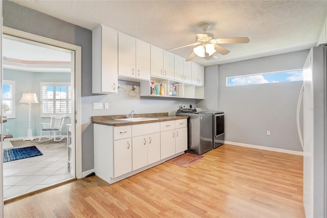 kitchen with sink, independent washer and dryer, stainless steel fridge, white cabinetry, and light hardwood / wood-style flooring