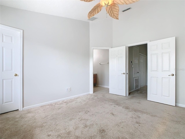 unfurnished bedroom with ceiling fan, light colored carpet, and a high ceiling