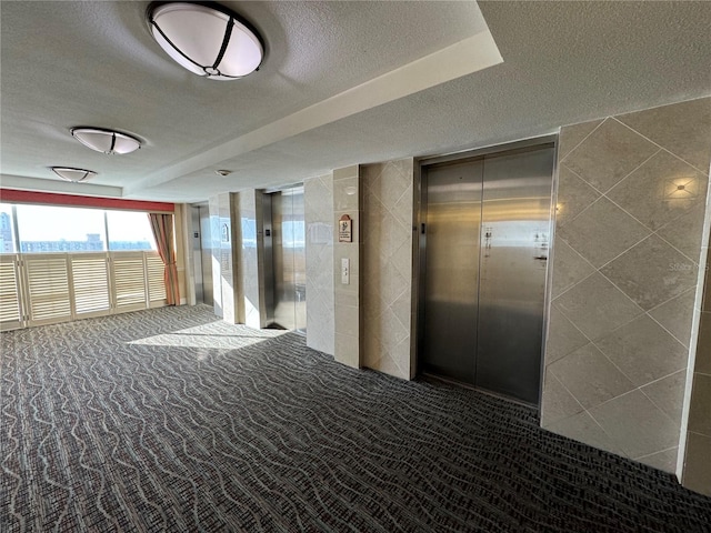 hall with a textured ceiling, elevator, and carpet