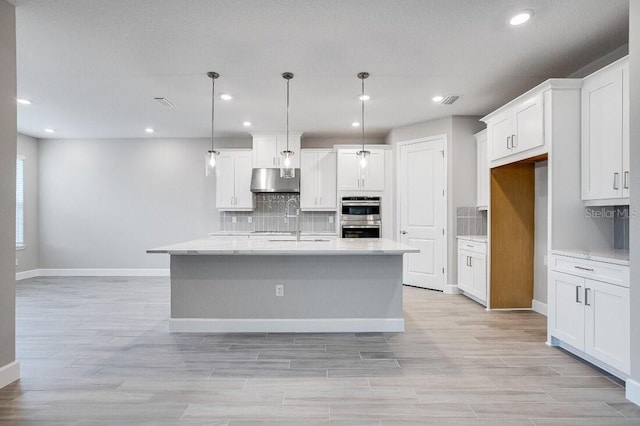 kitchen with pendant lighting, tasteful backsplash, an island with sink, sink, and white cabinets