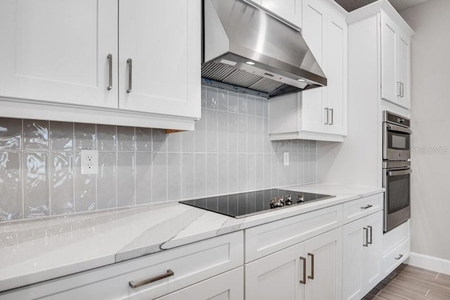 kitchen featuring black electric stovetop, light stone counters, stainless steel double oven, white cabinets, and range hood