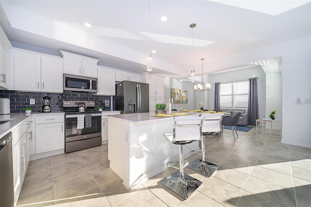 kitchen with appliances with stainless steel finishes, white cabinets, hanging light fixtures, and a kitchen island