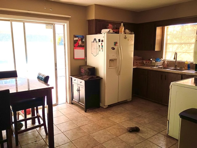 kitchen featuring washer / dryer, sink, light tile patterned flooring, white refrigerator with ice dispenser, and dark brown cabinetry