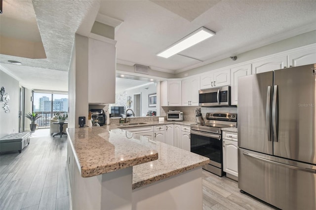 kitchen featuring appliances with stainless steel finishes, kitchen peninsula, a textured ceiling, and light stone countertops