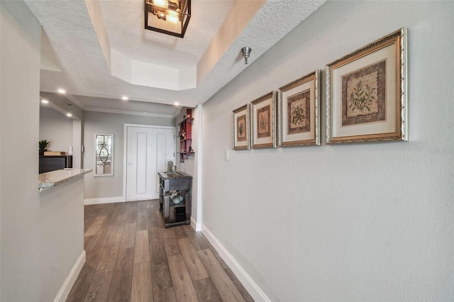 corridor featuring a textured ceiling, hardwood / wood-style flooring, and a tray ceiling