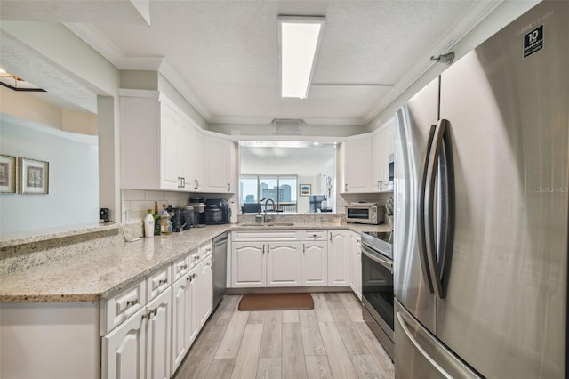 kitchen featuring kitchen peninsula, appliances with stainless steel finishes, white cabinetry, light hardwood / wood-style floors, and light stone counters