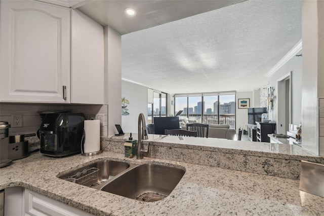 kitchen with light stone countertops, sink, white cabinets, and crown molding