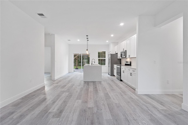 kitchen featuring light hardwood / wood-style flooring, an island with sink, white cabinets, decorative light fixtures, and appliances with stainless steel finishes