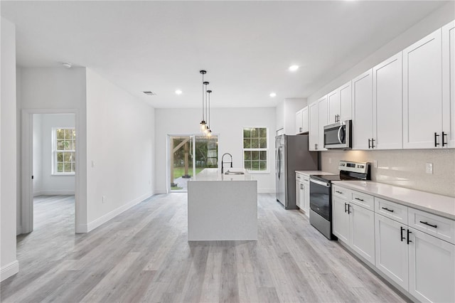 kitchen with white cabinets, hanging light fixtures, sink, light hardwood / wood-style floors, and stainless steel appliances