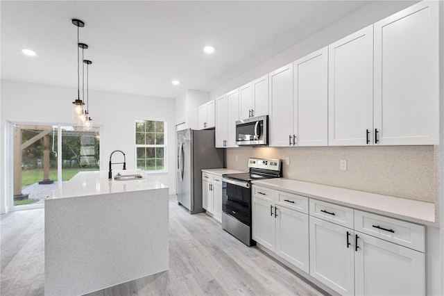 kitchen with white cabinets, an island with sink, stainless steel appliances, sink, and decorative light fixtures