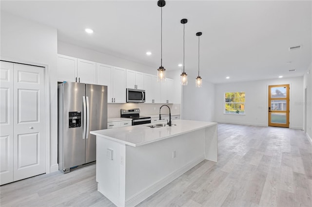 kitchen with a kitchen island with sink, sink, pendant lighting, appliances with stainless steel finishes, and light hardwood / wood-style floors