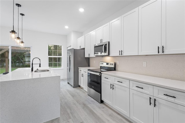 kitchen with appliances with stainless steel finishes, white cabinetry, light wood-type flooring, and pendant lighting