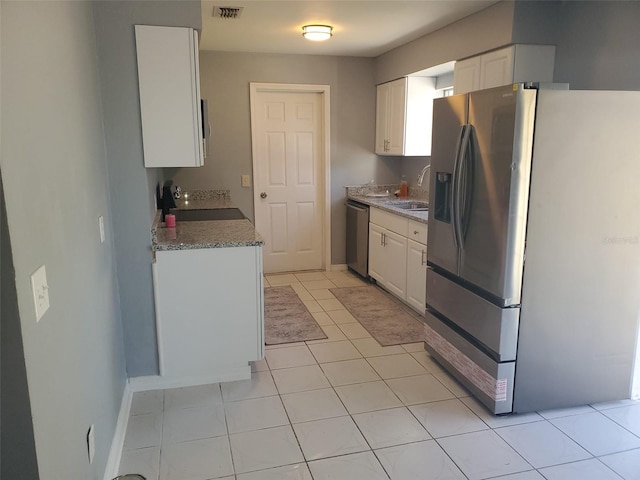 kitchen featuring sink, light tile patterned flooring, appliances with stainless steel finishes, white cabinets, and light stone counters