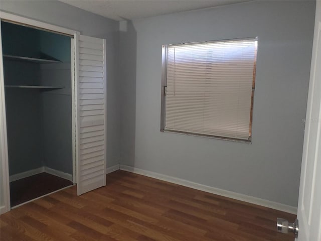 unfurnished bedroom with baseboards, a closet, and dark wood-style floors