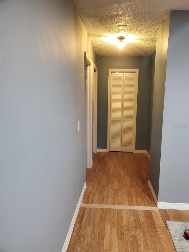 hallway featuring light wood-style floors, a textured ceiling, and baseboards