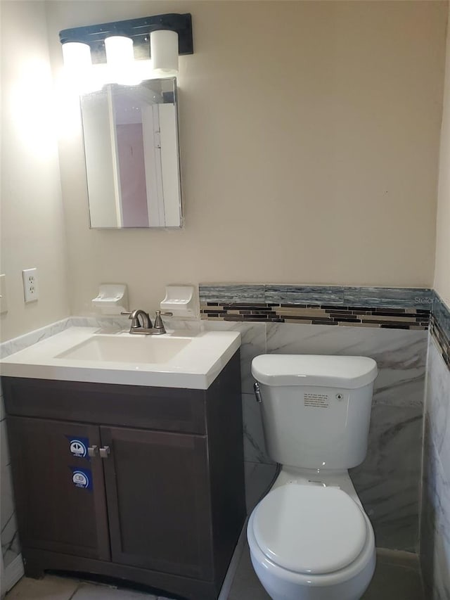 half bath with tile walls, toilet, vanity, and wainscoting