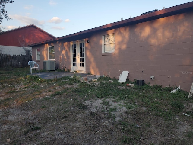 back of property with concrete block siding, french doors, central AC unit, and fence