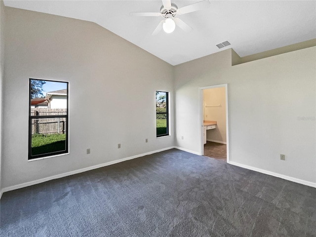 unfurnished bedroom featuring ceiling fan, dark colored carpet, vaulted ceiling, and ensuite bath