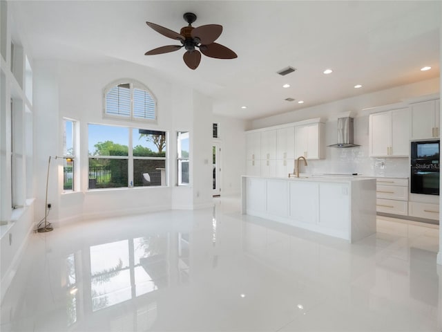 kitchen with white cabinets, light tile patterned floors, a kitchen island with sink, black appliances, and wall chimney exhaust hood