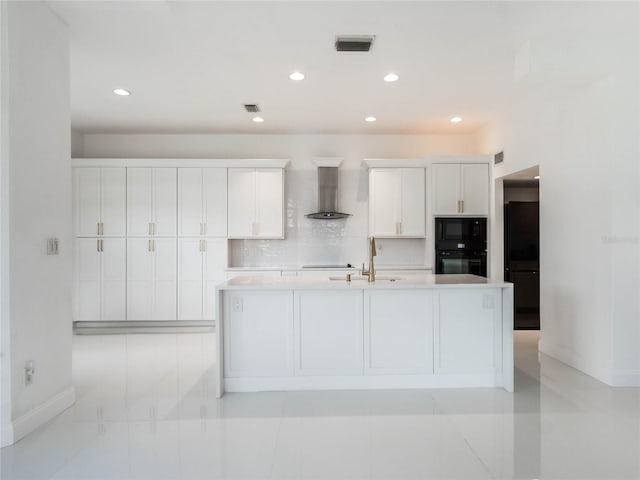 kitchen featuring wall chimney range hood, sink, black appliances, white cabinets, and a center island with sink