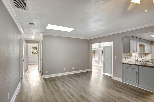 unfurnished living room featuring sink, ceiling fan, a skylight, and hardwood / wood-style floors