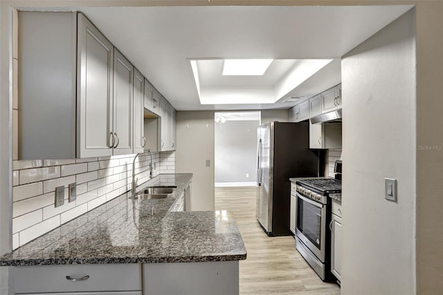 kitchen with a tray ceiling, dark stone counters, gas range, light hardwood / wood-style floors, and sink