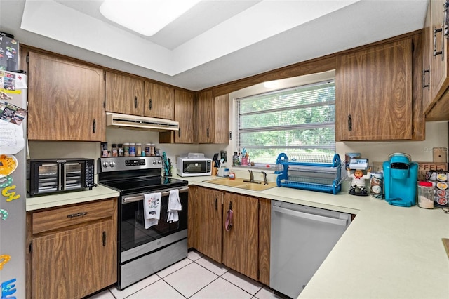 kitchen featuring stainless steel appliances, sink, light tile patterned flooring, a tray ceiling, and range hood