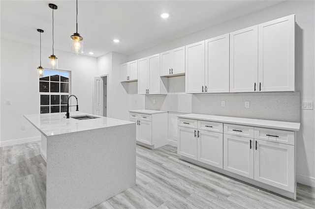 kitchen featuring sink, hanging light fixtures, white cabinets, light hardwood / wood-style flooring, and a center island with sink