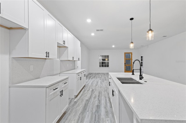 kitchen with white cabinetry, sink, hanging light fixtures, and light wood-type flooring