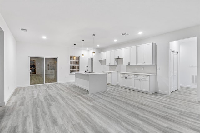 kitchen with white cabinets, a kitchen island with sink, light wood-type flooring, sink, and decorative light fixtures