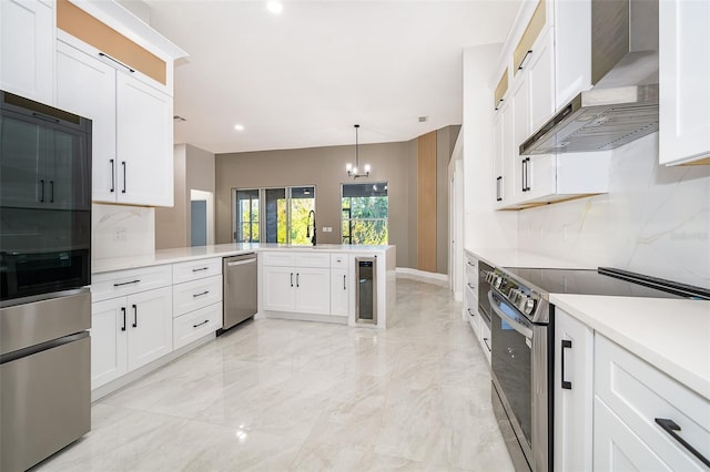 kitchen with wall chimney exhaust hood, kitchen peninsula, stainless steel appliances, wine cooler, and white cabinetry