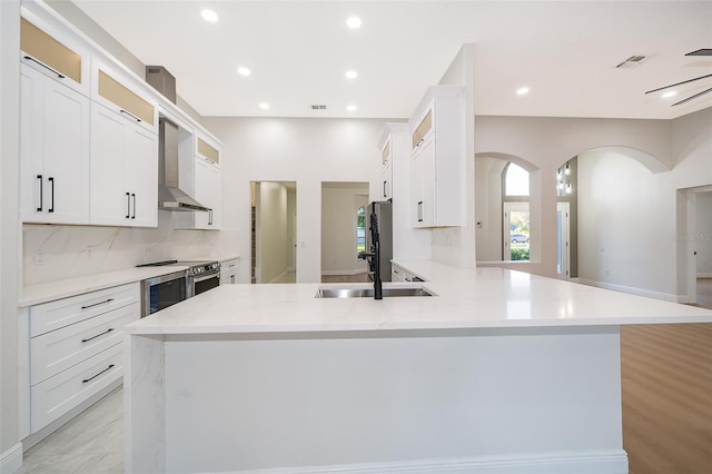 kitchen featuring wall chimney exhaust hood, white cabinets, kitchen peninsula, and tasteful backsplash