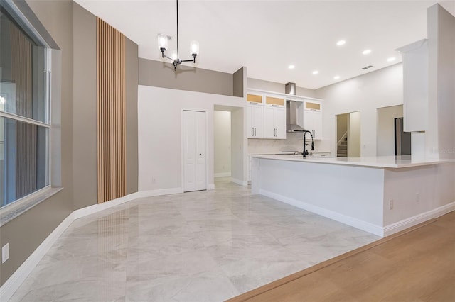 kitchen featuring wall chimney range hood, kitchen peninsula, decorative light fixtures, white cabinets, and a chandelier