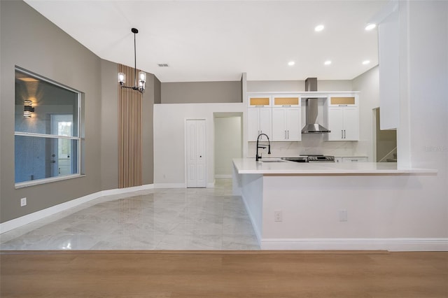 kitchen with wall chimney range hood, kitchen peninsula, decorative light fixtures, an inviting chandelier, and white cabinets