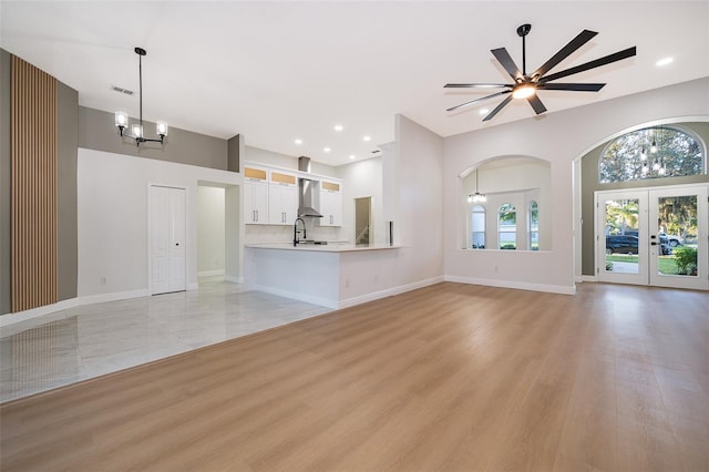 unfurnished living room featuring french doors, sink, light wood-type flooring, and ceiling fan with notable chandelier